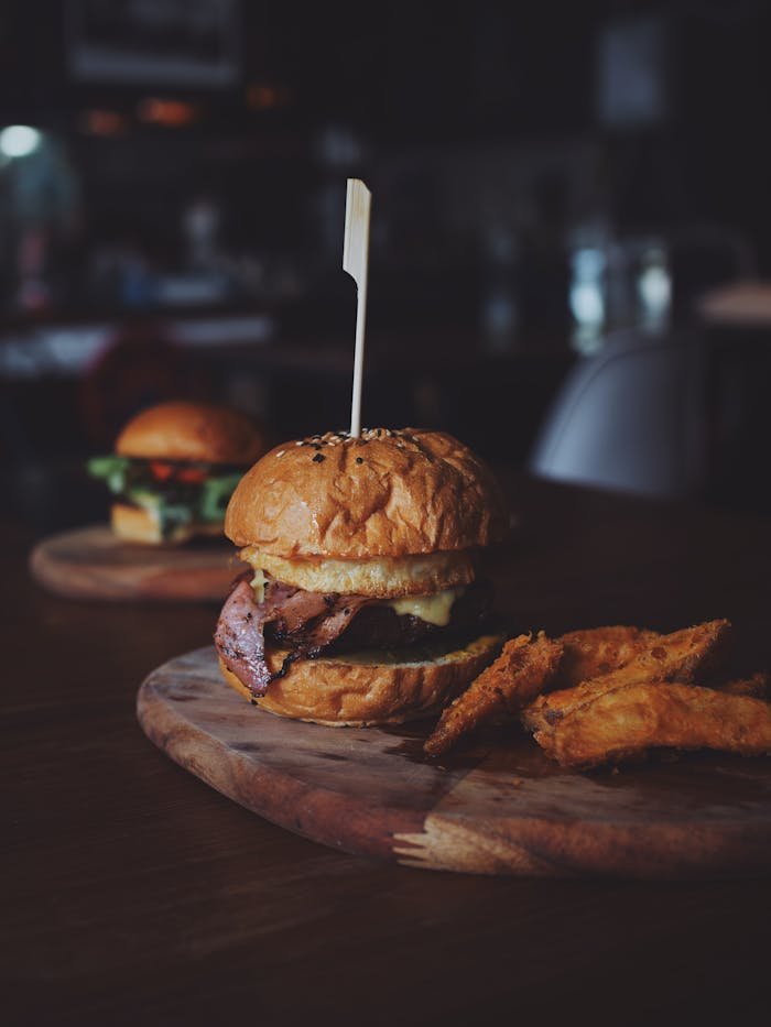 Home Delicious gourmet beef burger served with crispy sweet potato fries on a rustic wooden board.